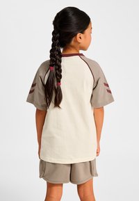 Baumwoll-T-Shirt mit beigem Körper und braunen Raglanärmeln mit kastanienbraunen Streifen, kombiniert mit passenden braunen Shorts. Weiche Textur, lässiges Design.