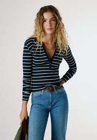 Námořnická a bílá pruhovaná dlouhá rukává košile Henley s knoflíkovým výstřihem, spárovaná se světle modrými džíny a hnědým opaskem.