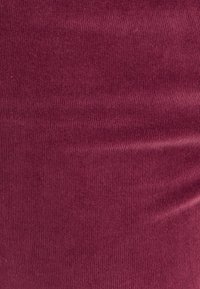 Bordeaux ribbelstof met verticale lijnen, met een zachte textuur. Het materiaal lijkt rekbaar en lichtgewicht, geschikt voor diverse toepassingen.