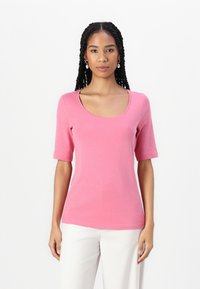 Rövid ujjú, rózsaszín T-shirt, puha pamutból készült, kivágott nyakkivágással és testhezálló kialakítással, fehér nadrággal párosítva.