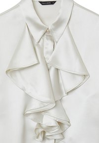 Seidenbluse in Off-White mit spitzem Kragen und großen Rüschendetails vorne. Mit einem Knopfverschluss am Kragen.