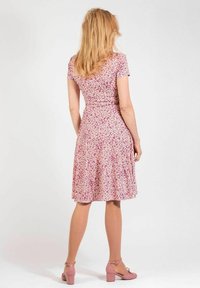 Kukkakuosisella mekolla vaaleanpunaisissa sävyissä, jossa on lyhyet hihat ja levenevä hameosa. Sileä kangas, jossa on vartalonmyötäinen vyötärö, yhdistettynä vaaleanpunaisiin kenkiin.