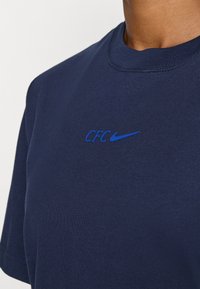 Mörkblå bomulls t-shirt med rund halsringning, prydd med "CFC" och en Nike swoosh-logotyp i kontrasterande blått på bröstet.