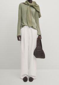 Maglione verde chiaro con texture, sciarpa, pantaloni bianchi a gamba larga e una borsa in suede marrone scuro con dettagli geometrici.