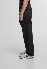 Zwarte cargobroek met een relaxte pasvorm, voorzien van zijzakken en een versleten textuur. Gecombineerd met metallic grijze hardloopschoenen.