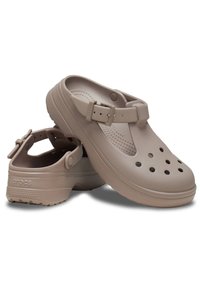 Le zoccoli Crocs di color marrone chiaro presentano una silhouette arrotondata, fori di ventilazione, una fascia regolabile e un fondo testurizzato. Realizzati in materiale durevole e flessibile.