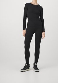 Maglietta nera a maniche lunghe e leggings aderenti realizzati in materiale elasticizzato, abbinati a scarpe sportive nere con suola bianca e dettagli del logo.
