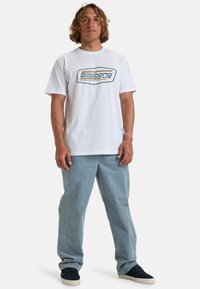 T-shirt en coton blanc avec un logo Billabong multicolore sur le devant. Associé à un pantalon en denim bleu clair et des baskets navy.