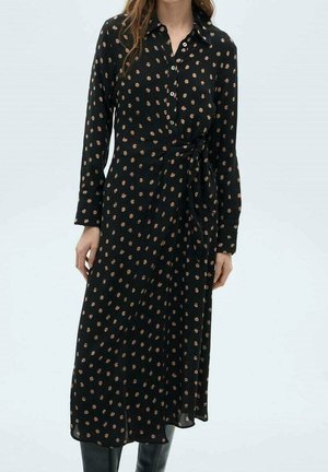 Robe midi noire à manches longues avec des pois beige, boutonnée sur le devant, col, ceinture à la taille, portée avec des bottes noires montant jusqu'aux genoux.