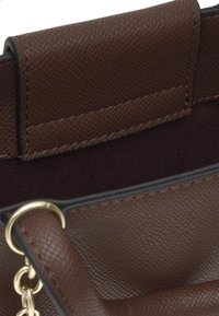 Wnętrze brązowej torebki ze skóry o fakturze z czarną podszewką z tkaniny oraz złotym metalowym pierścieniem i łańcuszkiem na pasku.