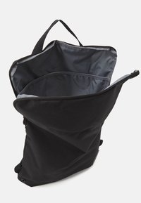 Sort stof rygsæk med lynlåse på toppen, der har et rummeligt interiør, minimalistisk design og et enkelt greb på toppen. Glat tekstur.