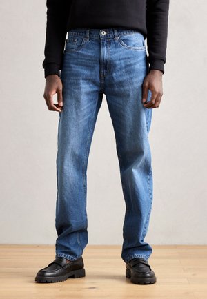 Jeans din denim de culoare albastru deschis, cu o croială dreaptă, design cu cinci buzunare și decolorare subtilă. Combinat cu pantofi negri slip-on cu tălpile texturate.