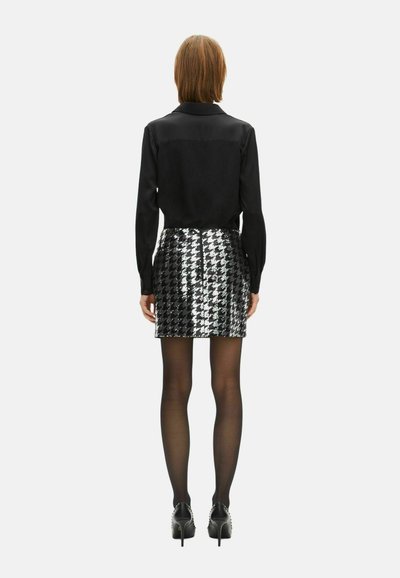 Blusa nera con maniche lunghe, abbinata a una mini gonna a motivi houndstooth metallici. Indossata con collant neri trasparenti e scarpe con tacchi.