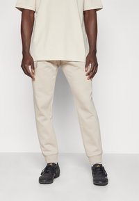 Beige Oversized-T-Shirt kombiniert mit passenden beigen Sweatpants. Schwarze Sportschuhe mit strukturierter Oberfläche und Schnürsenkeln. Schlichter, lässiger Stil.