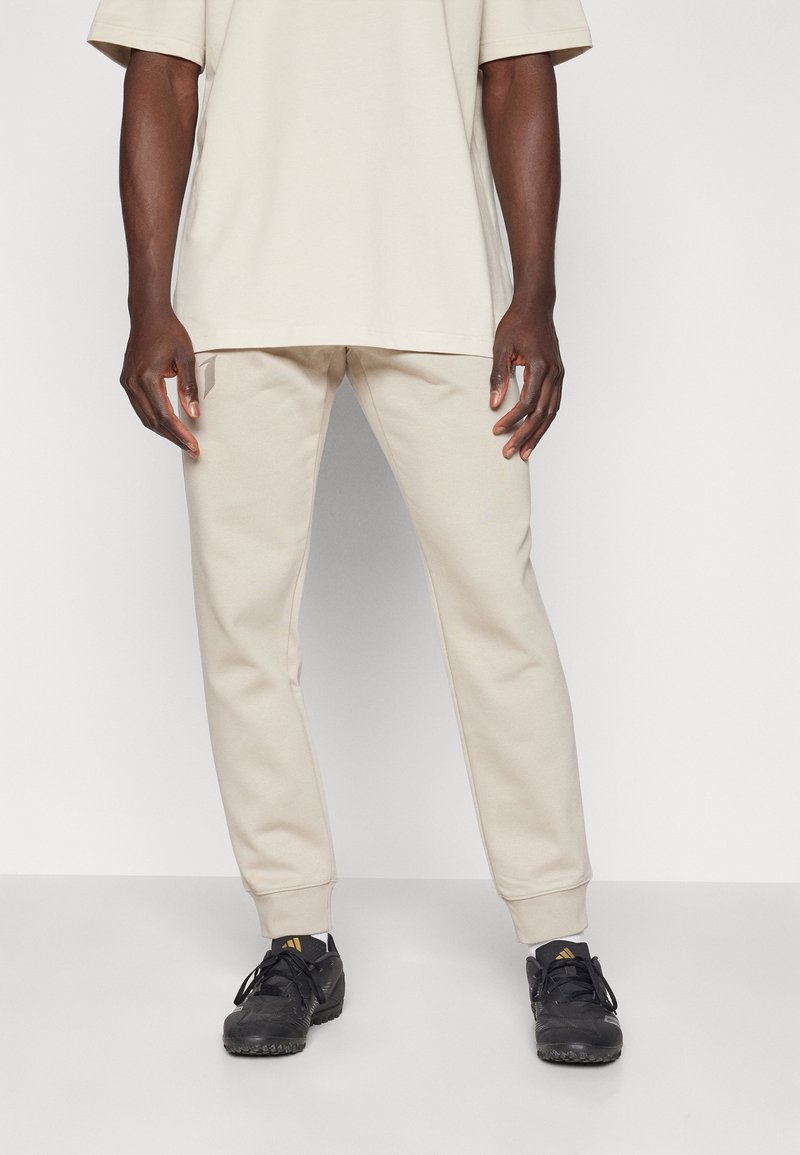Beige Oversized-T-Shirt kombiniert mit passenden beigen Sweatpants. Schwarze Sportschuhe mit strukturierter Oberfläche und Schnürsenkeln. Schlichter, lässiger Stil.