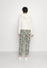 Kremowa polarowa bluza z kapturem, z troczkami, w zestawie z zielonymi spodniami cargo w kamuflażu z elastycznymi mankietami i kieszeniami. Założone z białymi trampkami.