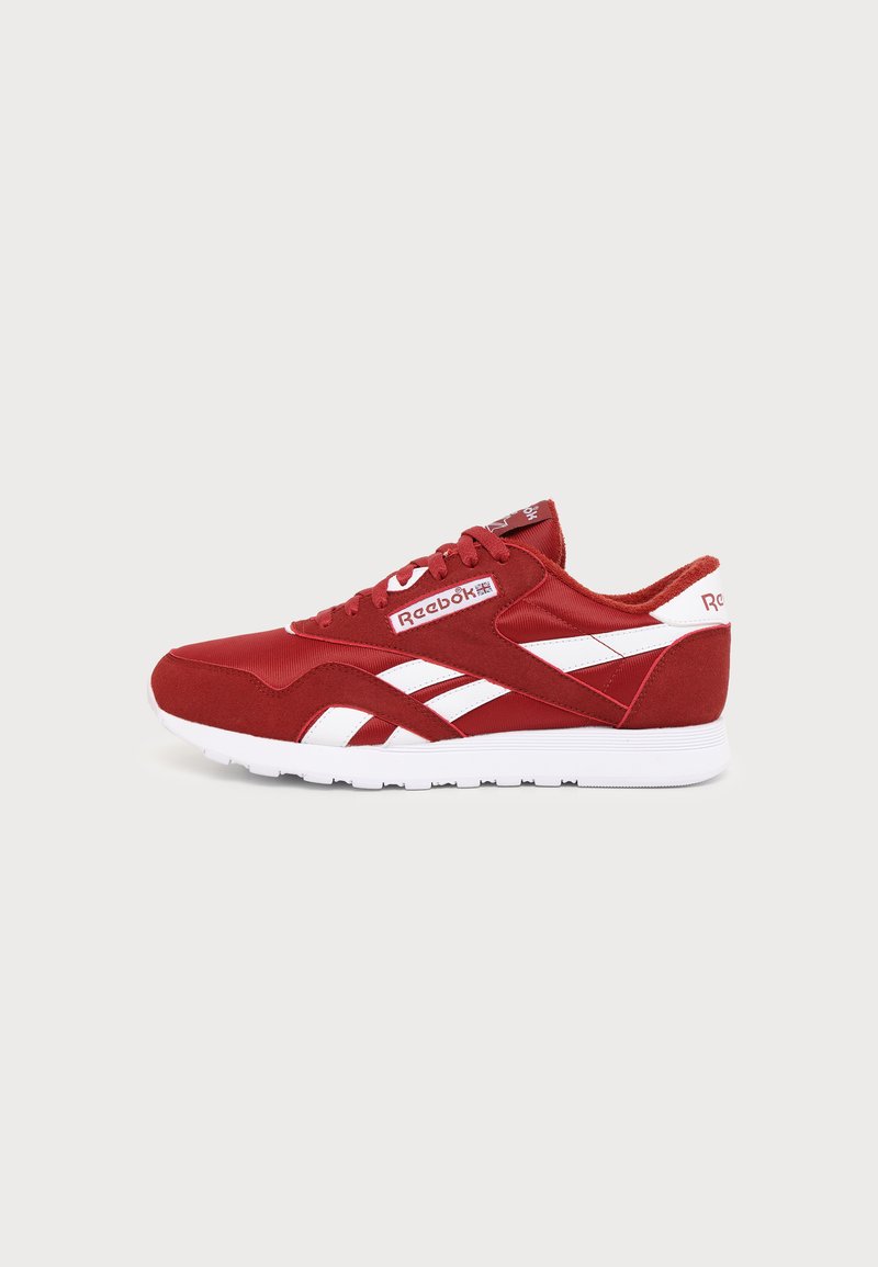 Κόκκινο και λευκό αθλητικό παπούτσι Reebok με κορδόνια, λογότυπο στο πλάι και τη φτέρνα, και λευκή λαστιχένια σόλα, εμφανίζεται από το πλάι σε μονόχρωμο φόντο.