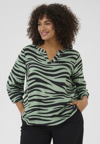 Blusa a righe verdi e nere con scollatura a V e maniche lunghe, caratterizzata da una vestibilità ampia e polsini arricciati per un tocco di originalità.