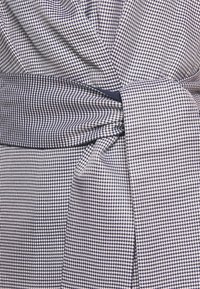 Látka s námorně modrým a bílým vzorem houndstooth svázaná uzlem v pase, ukazující podrobnou strukturu a těsné tkaní.