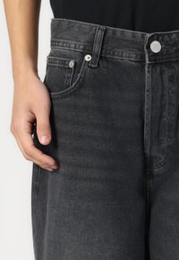 Mustat denim-farkut suoralla istuvuudella, joissa on napitus, viisi taskua ja näkyvät ompeluyksityiskohdat. Sujuva rakenne.