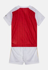 Jersey rojo con patrón de zigzag en la parte posterior, mangas blancas y pantalones cortos blancos con acentos dorados. Hecho de material atlético ligero.