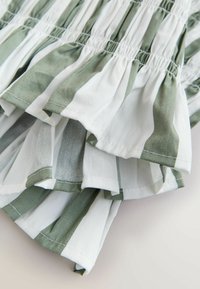 Material alb și verde cu dungi verticale, elastic adunat și margini cu volănașe suprapuse.