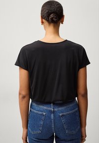 Sort kortærmet top med rund halsudskæring og en glat tekstur, parret med højtaljede blå denim jeans med baglommer.