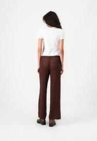 Pantalones de punto marrones de pierna ancha con un acabado texturizado, combinados con una camiseta blanca de manga corta y botines negros.