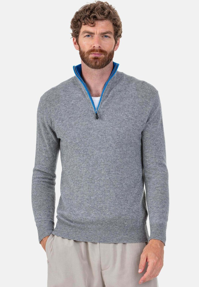 Pull en tricot gris avec une fermeture éclair quart de longueur et un accent bleu le long du col, manches longues et ourlet côtelé. Texture douce.