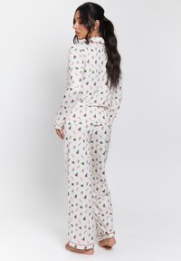 Witte pyjama set met een feestelijk patroon van gemberbroodmannen, zuurstokken en kerstbomen; zachte stof met contrasterende piping details.