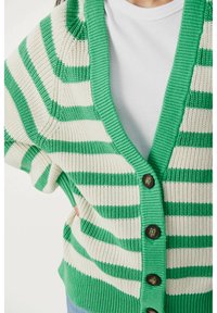 Cardigan a righe verdi e crema con scollo a V, maniche corte e cinque bottoni marroni sul davanti, realizzato in un tessuto a maglia testurizzato.