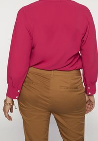 Fuchsia long-sleeve blouse with buttoned cuffs paired with tan trousers featuring back pockets and straight leg design.