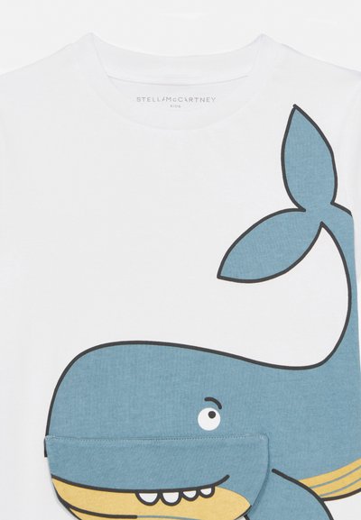 Balta bērnu krekls ar lielu zilu vaļu grafiku, kurā ir acs un zobi, un locījums, kas rada 3D mutes efektu.