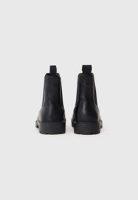 Sorte læder Chelsea-støvler med rund tå, kraftig gummisål og stropper ved hælen. Glat tekstur og minimalistisk design.