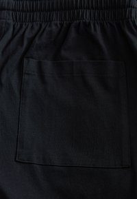 Nahaufnahme eines schwarzen Stoffes mit einer aufgenähten quadratischen Tasche unter einem elastischen Bund.