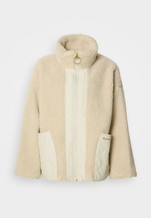 Kreemika värvi fliisjope kõrge kraega, tikanddetailidega ja kuldse riistvaraga lukul. Varustatud kahe küljetaskuga.