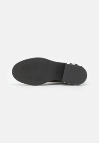 Suela de zapato negra, textura suave, forma ligeramente curvada. Presenta un área acolchada cerca del talón y lunares blancos en contraste a los lados.