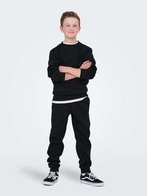 Hanorac negru cu guler rotund, asociat cu pantaloni de trening negri. Material texturat, croială lejeră și accente albe. Adidași negri completează ținuta.