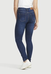 Slim-fit, mörkblå denimjeans med medelhög midja, femfickdesign och kontrasterande sömmar; bärs med vita sneakers.