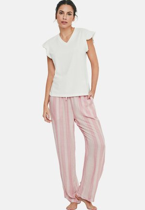 Femme debout, pieds nus, portant un haut blanc à manches courtes avec un col en V et un pantalon rose ample à rayures blanches verticales.