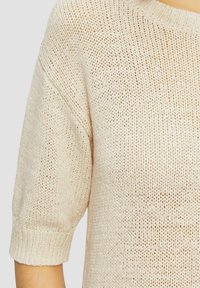 Beige neulepaita lyhyillä hihoilla, jossa on löysä kudontamalli ja leveä kaula-aukko, valmistettu kevyestä ja hengittävästä materiaalista.