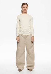Blusa de manga larga color crema con detalles fruncidos, combinada con pantalones beige de pierna ancha que presentan una textura suave y costuras a medida.