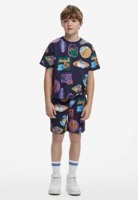 Completo con maglietta corta viola e pantaloni shorts, caratterizzato da stampe grafiche colorate. Realizzato in tessuto morbido, con un fit rilassato e life elasticizzato.
