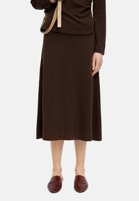 Brązowa bluzka z długim rękawem w zestawieniu z pasującą brązową spódnicą do kostek. Miękka tkanina o gładkiej fakturze. Ubrane z bordowymi butami wsuwanymi.