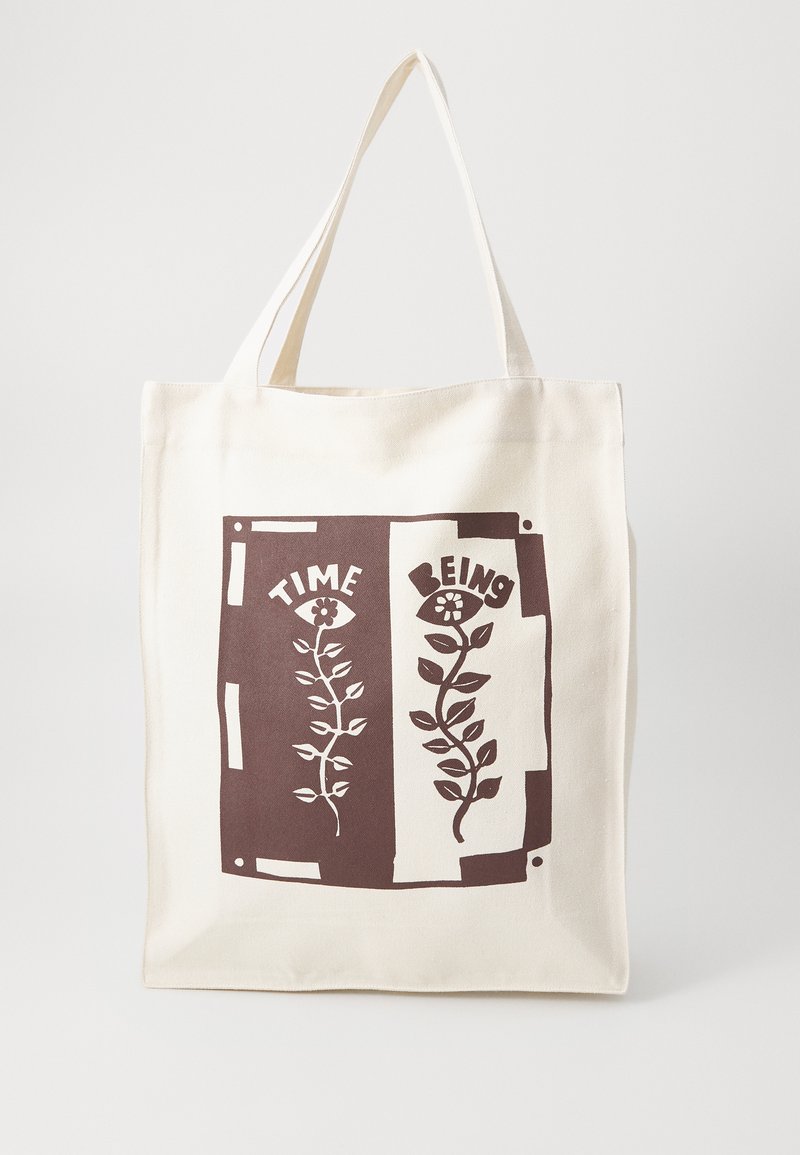 Canvas tote bag with cream fabric and brown graphic design featuring flowers and the words "TIME" and "BEING" on two separate panels.