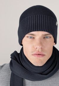 Navy ribbed knit beanie and scarf set. The beanie features a close-fitting design, while the scarf is thick and textured. Both have a smooth finish.
