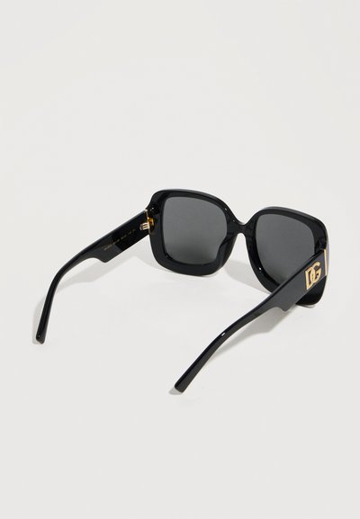 Μαύρα τετράγωνα γυαλιά ηλίου μεγάλης διάστασης με σκοτεινούς φακούς και χρυστό λογότυπο DG στα πλαϊνά, απεικονισμένα σε λευκό φόντο.