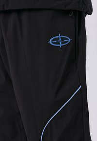 Pantalones negros hechos de un tejido ligero, con un logo azul y un ribete azul a lo largo de las costuras laterales. Textura suave, diseño moderno.
