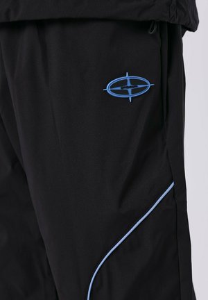 Zwarte broek van lichtgewicht stof, met een blauw logo en blauwe piping langs de zijnaad. Soepele textuur, modern ontwerp.