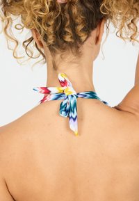 Halter in seta colorato con legatura sul retro del collo, caratterizzato da motivi blu, giallo, rosso e viola. Texture liscia, dettaglio decorativo a nodo.
